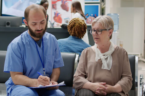 A nurse consults with a patient in a hospital waiting area.