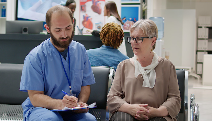 A nurse consults with a patient in a hospital waiting area.